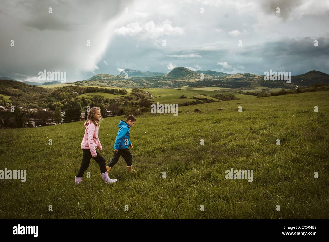 Siblings on a walk in spring nature, rain clouds on sky. Wearing rain ...