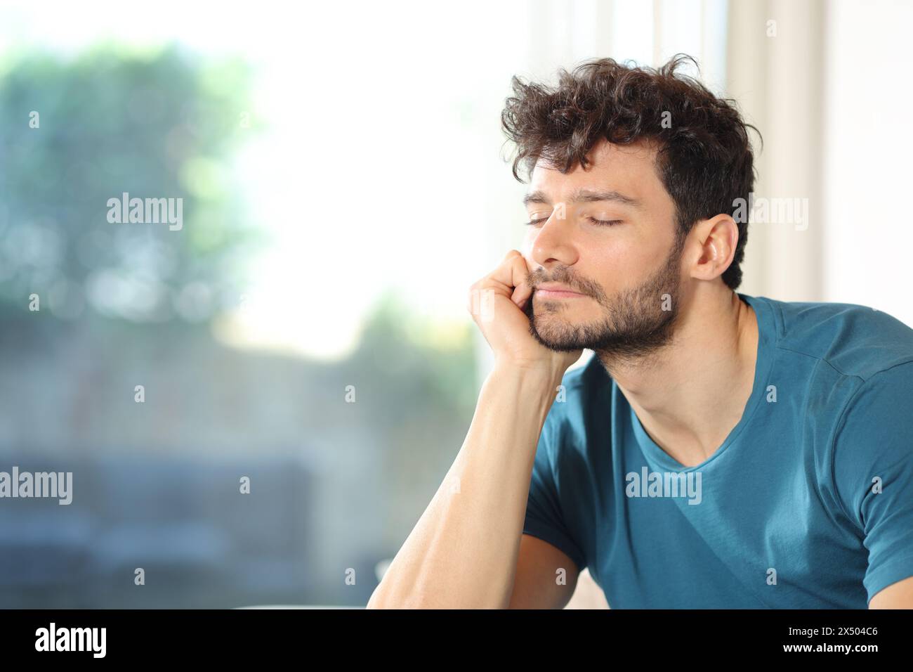 Satisfied man relaxing near a window at home Stock Photo