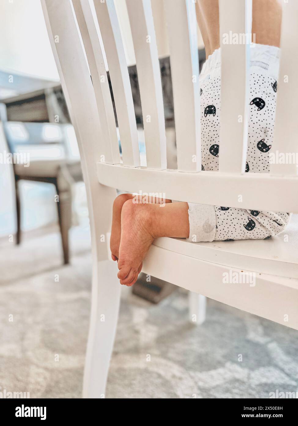 Close-up side view of a barefoot toddler kneeling on a chair Stock Photo