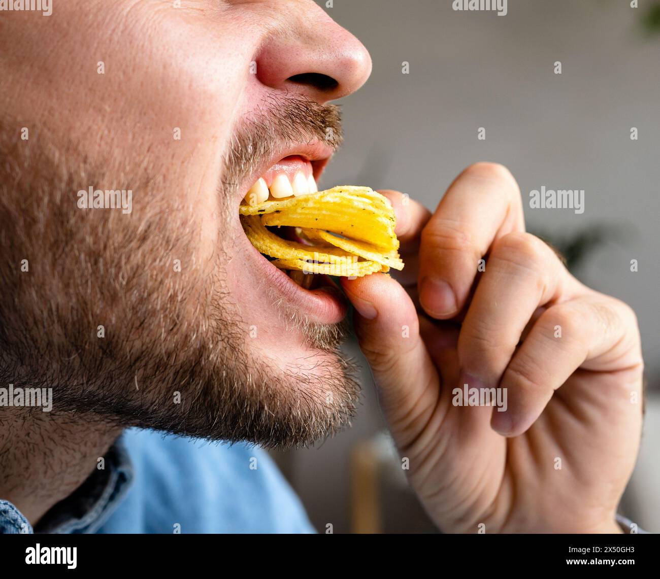 Man eats chips, closeup photo of the eating mouth. Unhealthy eating. Stock Photo