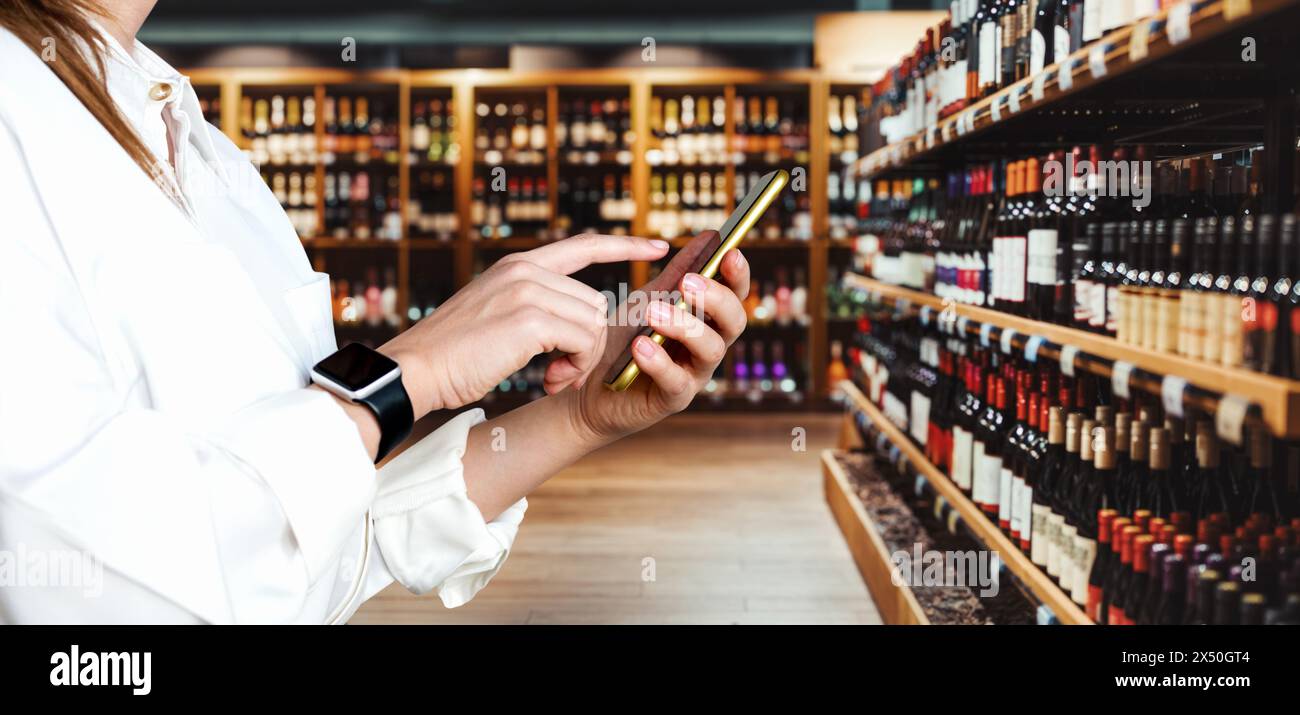 Businessperson using smartphone in liquor store. E-commerce and retail. Selling wine online. Internet ordering of wine and alcohol product. Stock Photo