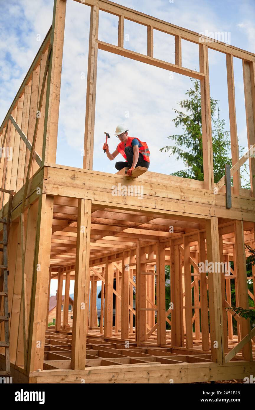 Wooden two-story frame house being built by carpenter. Man wearing ...