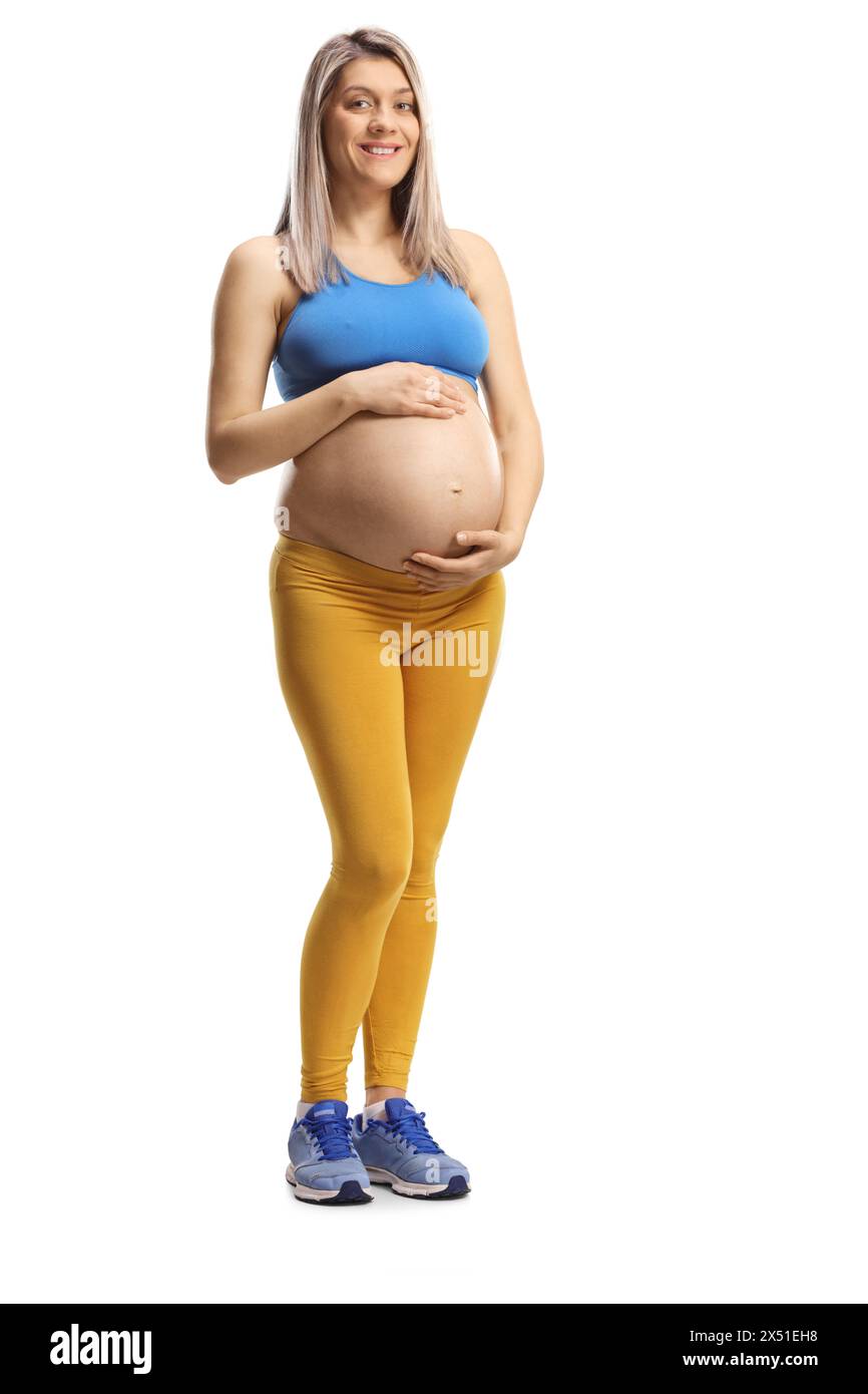 Full length portrait of a pregnant woman in sportswear holding her belly isolated on white background Stock Photo