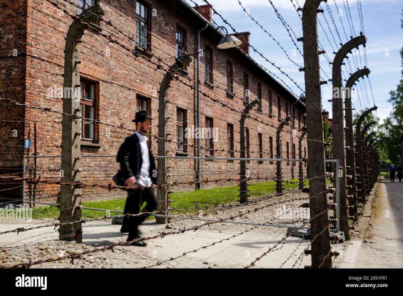 Visitor walks past wired fence as he arrives for the March of the Living 2024 at Auschwitz Camp gate 'Work Makes you Free' with 55 holocaust survivors on May 06, 2024 in O?wi?cim, Poland. Holocaust survivors, and October 7th survivors attend the March of the Living together with a delegation from, among others, the United States, Canada, Italy, United Kingdom. On Holocaust Memorial Day observed in the Jewish calendar (Yom HaShoah), thousands of participants march silently from Auschwitz to Birkenau. The march has an educational and remembrance purpose. This year March was highly politicized d Stock Photo