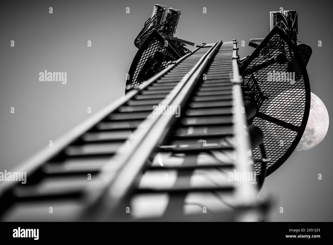 Looking up a lattice mast with installed telecommunication equipment. Full moon behind grid on top of mast. Black and white impression. Stock Photo