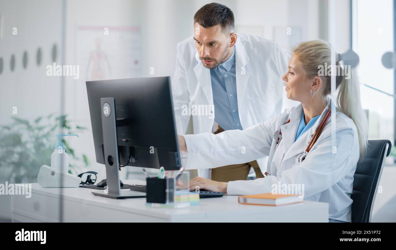 Hospital Medical Doctor's Office: Two Professional Physicians Talking, Consulting and Working on Computer. Specialists Discuss Patient Online Treatment, Writing Digital Medicine Prescriptions Stock Photo