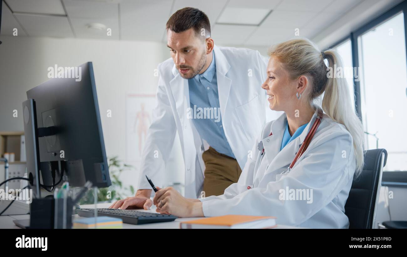 Hospital Medical Doctor's Office: Two Professional Physicians Talking, Consulting and Working on Computer. Specialists Discuss Patient Online Treatment, Writing Digital Medicine Prescriptions Stock Photo
