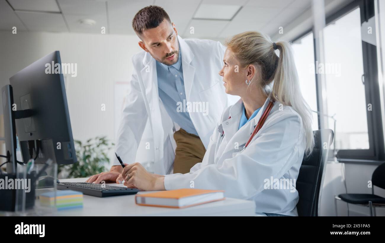 Hospital Medical Doctor's Office: Two Professional Physicians Talking, Solving Problem, Working on Computer. Specialists Discuss Patient Online Treatment, Writing Digital Medicine Prescriptions Stock Photo