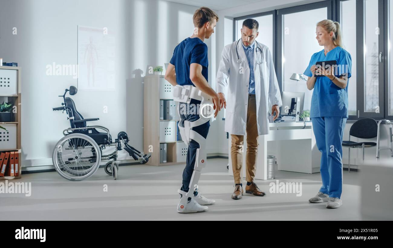 Hospital Physical Therapy: Doctor and Rehabilitation Specialist Use Tablet Computer, Helps Disabled Patient with Injury Walks while Wearing Advanced Robotic Exoskeleton Legs. Advanced Physiotherapy Stock Photo