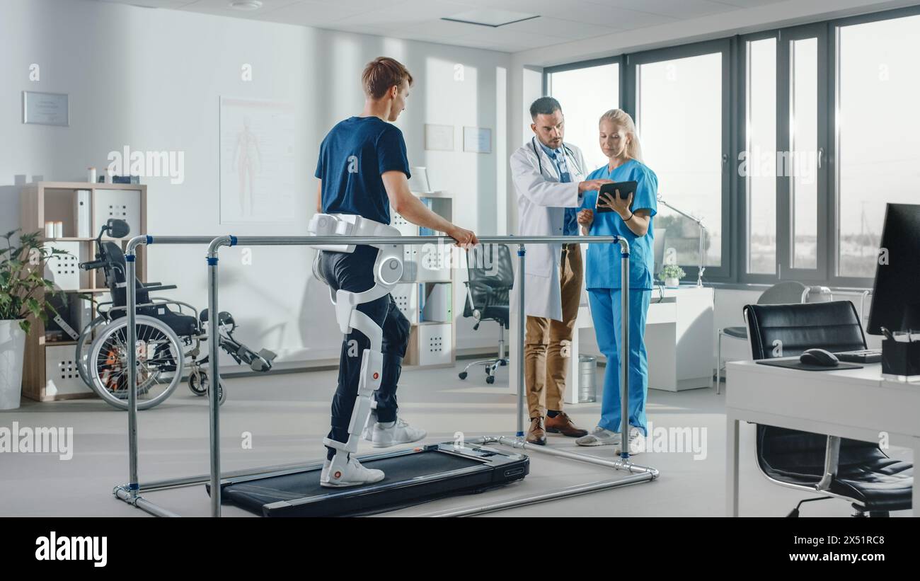 Modern Hospital Physical Therapy: Patient with Injury Walks on Treadmill Wearing Advanced Robotic Exoskeleton. Physiotherapy Rehabilitation Scientists, Engineers, Doctors Help Disabled Person Stock Photo