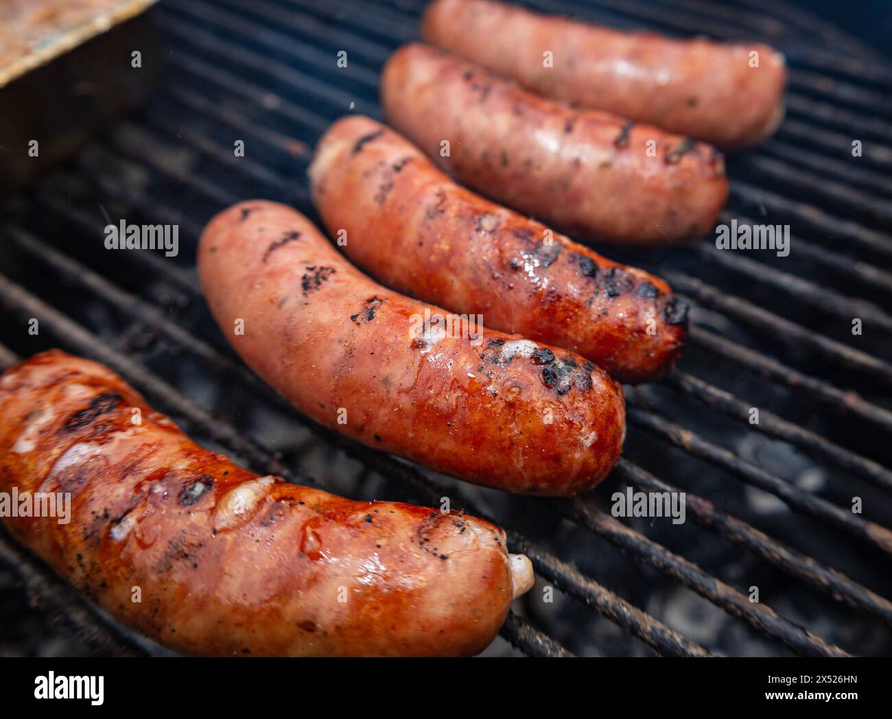 Five sausages grilling on an outdoor barbecue with visible char marks. A mouth-watering image ideal for food, grilling, BBQ, and summer-themed content Stock Photo