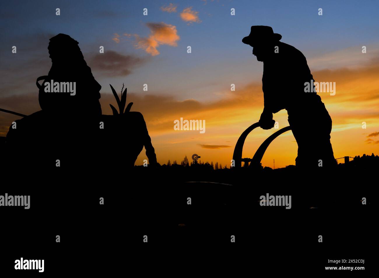 As the sun sets, a silhouette of a man and a woman toil the land together, embodying the harmony of partnership and the essence of rural life Stock Photo