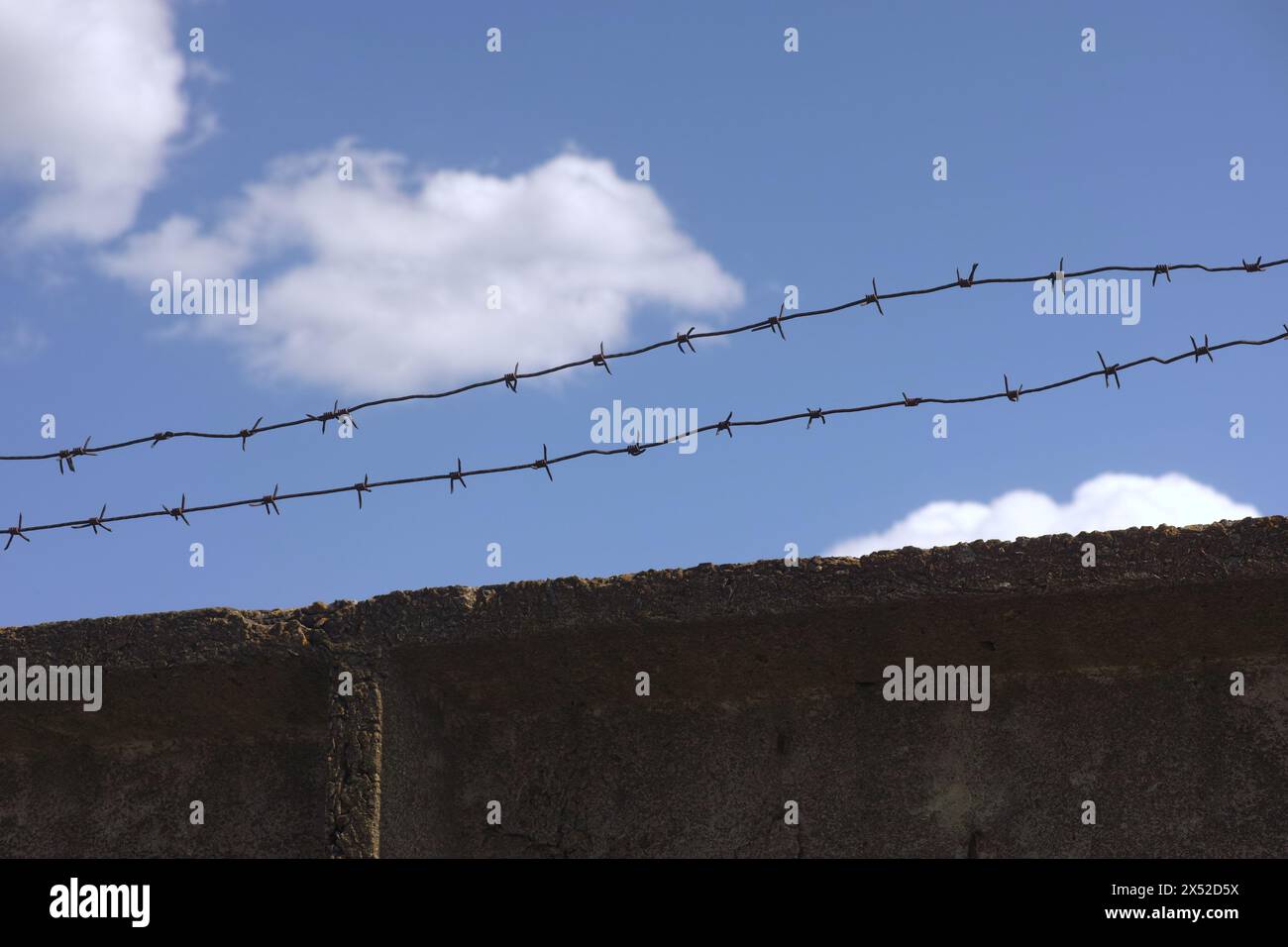 A concrete wall with barbed wire on top against a blue sky background ...