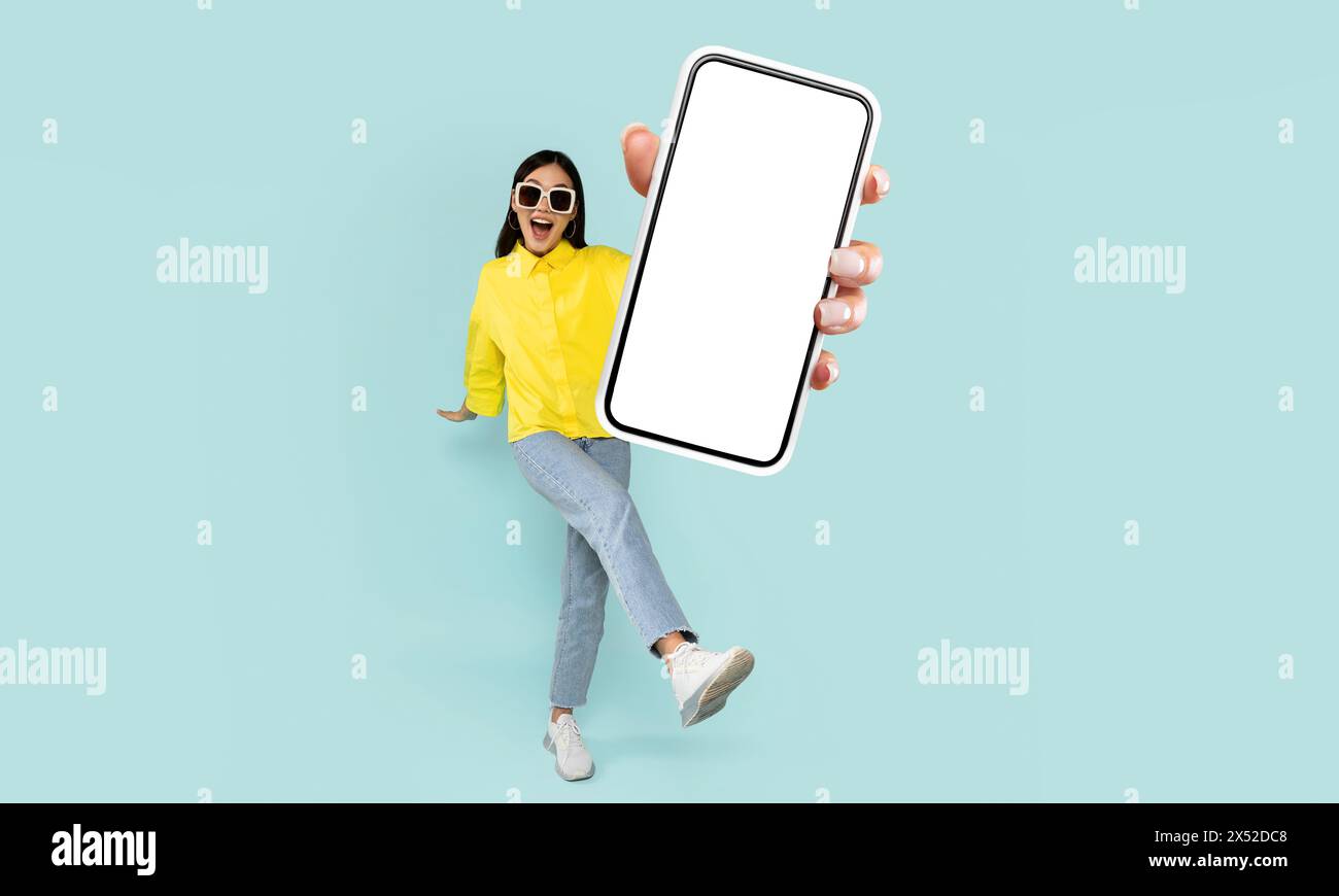 Woman in Yellow Shirt Presenting Smartphone With Blank Screen Stock Photo