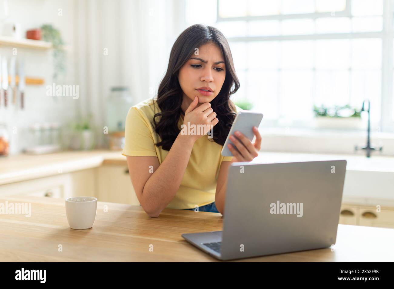 Pensive Young Woman Using Smartphone While Working on Laptop Stock Photo