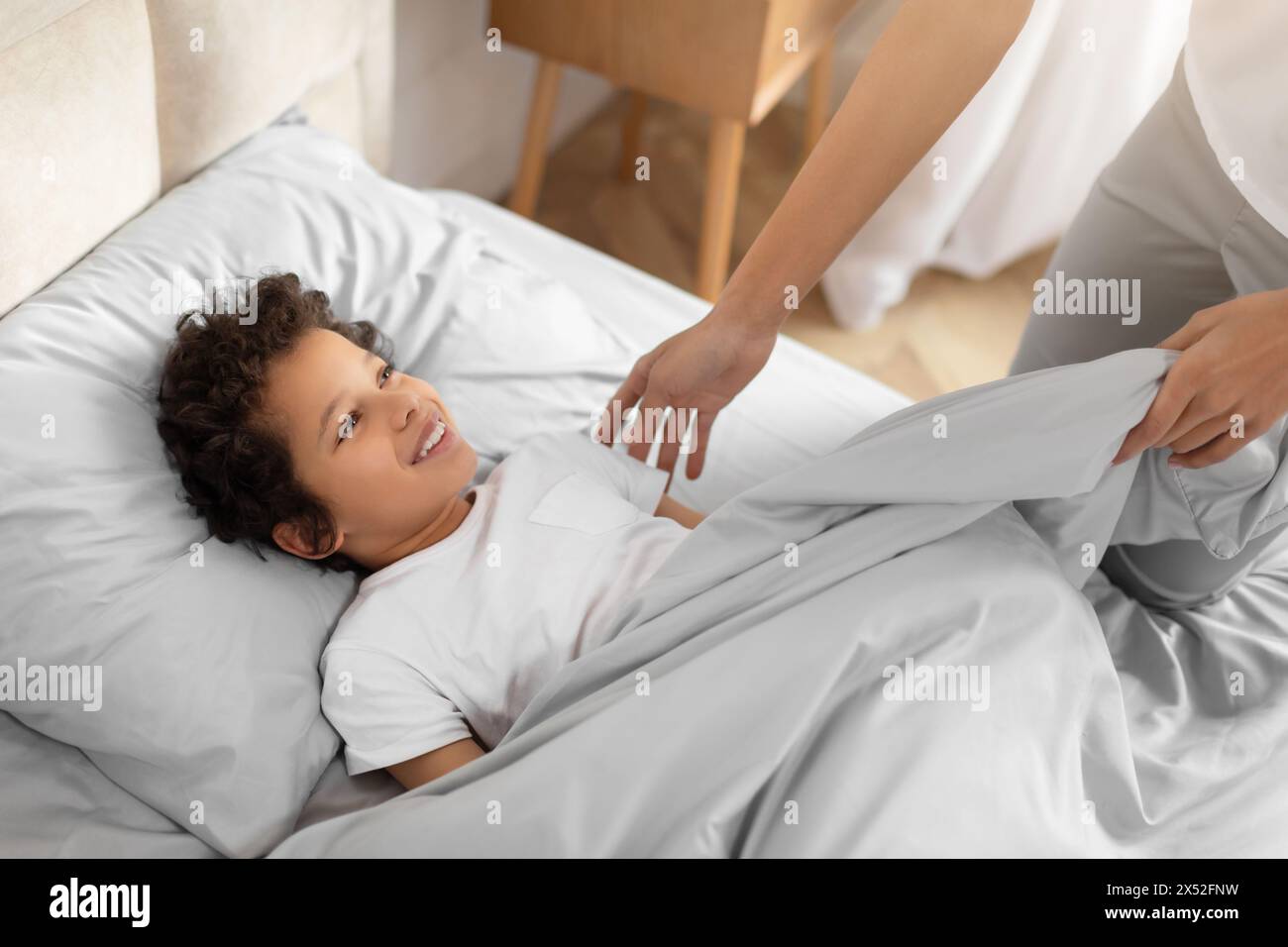 Smiling Child Lying in Bed Being Tucked In by Parent Stock Photo