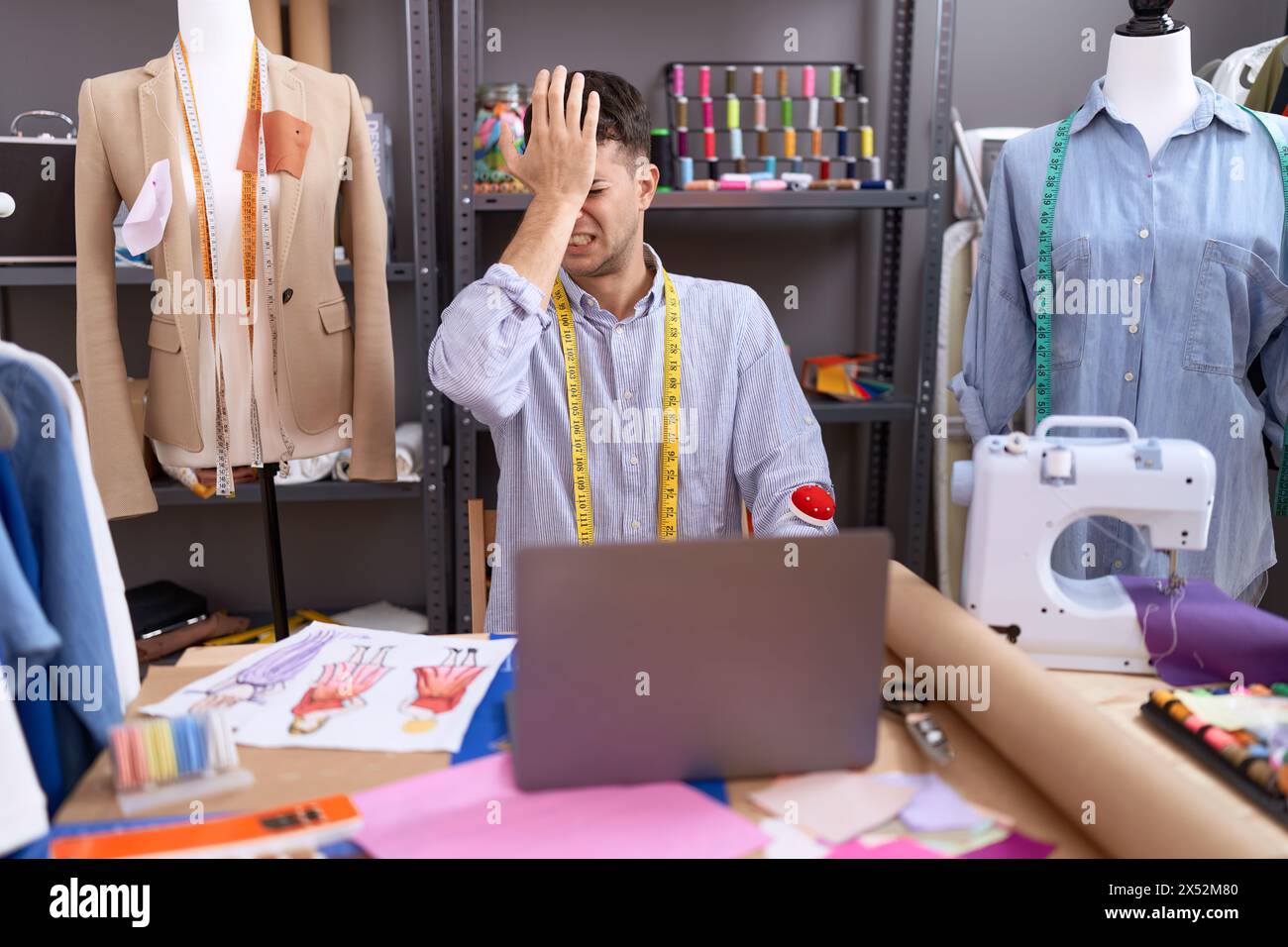 Young hispanic man dressmaker designer using laptop surprised with hand ...
