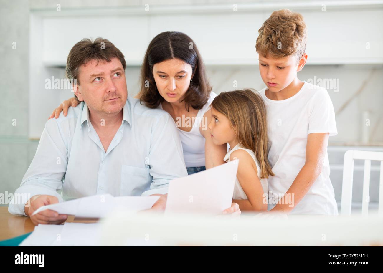 Wistful father looking through papers with family Stock Photo - Alamy