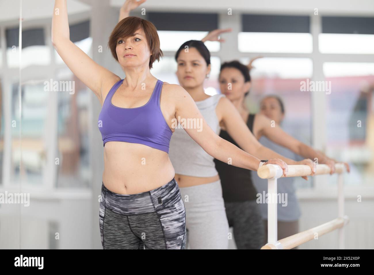 Female amateurs stand in third position near ballet barre during group ...