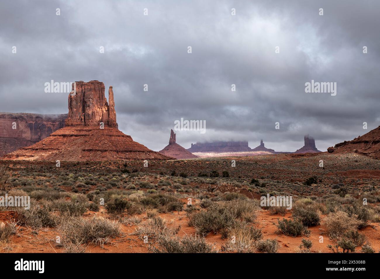 Low rainclouds hug a butte in Monument Valley's Navajo Tribal Park as rain hydrates the dry desert terrain. Stock Photo