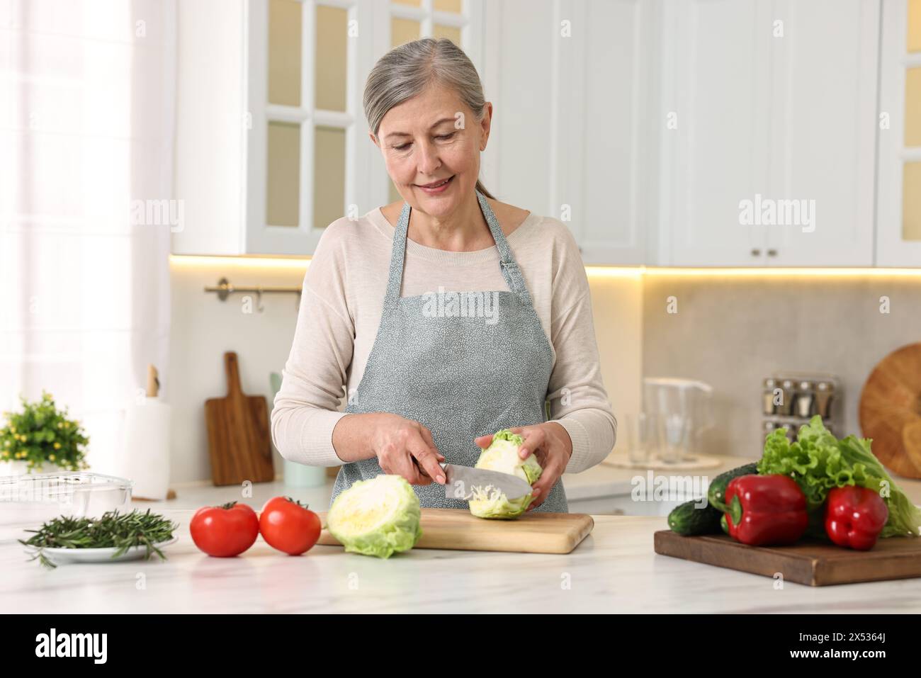 Happy housewife cutting cabbage at table in kitchen Stock Photo