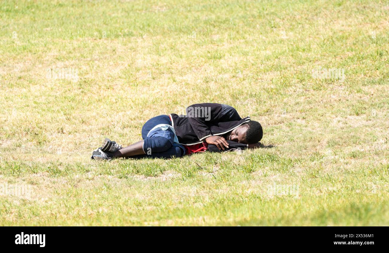 black African homeless man lying on the grass sleeping concept economic hardship or hard times in South Africa with copy space Stock Photo