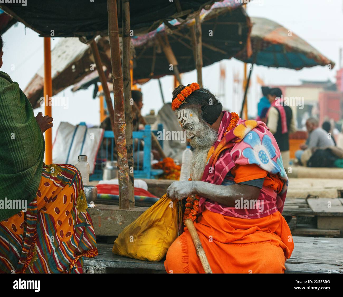 Brightly dressed sadhu or spiritual aspirant  sitting on a puja platform in Varanasi, India. Stock Photo