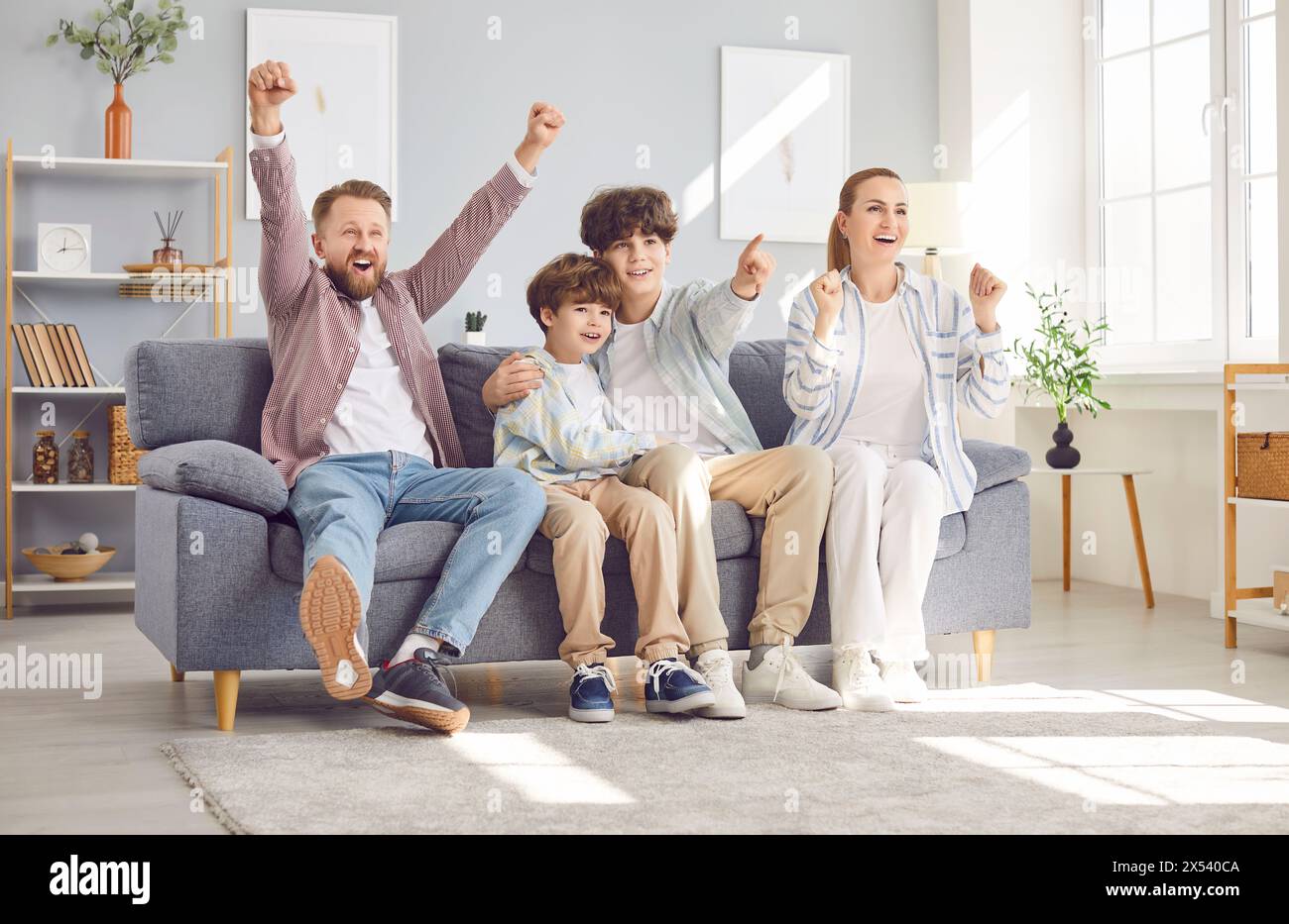 Portrait of excited happy family of four with children boys watching football on tv at home. Stock Photo