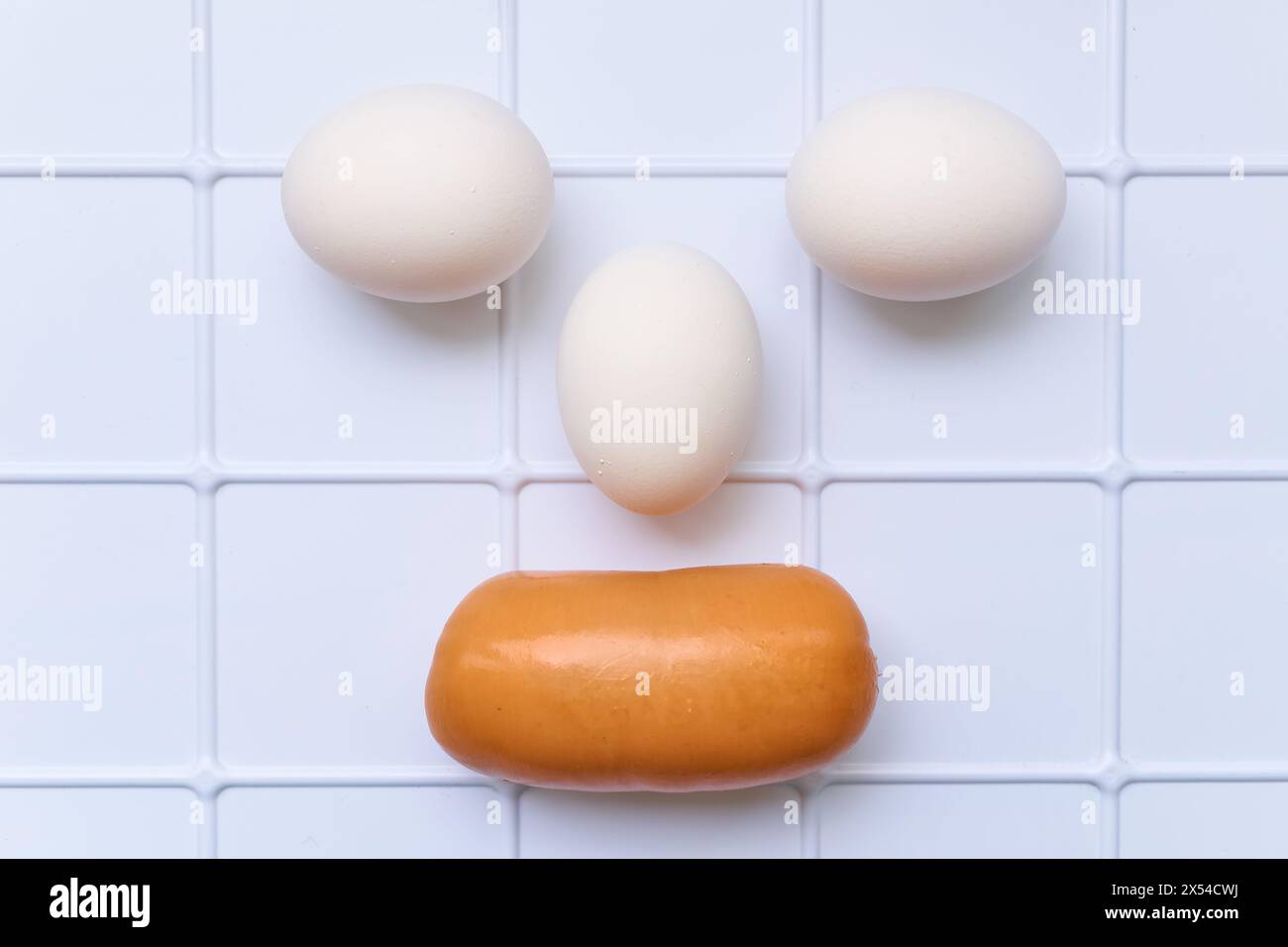 Comic face of three eggs and sausages on a plastic checkered surface Stock Photo