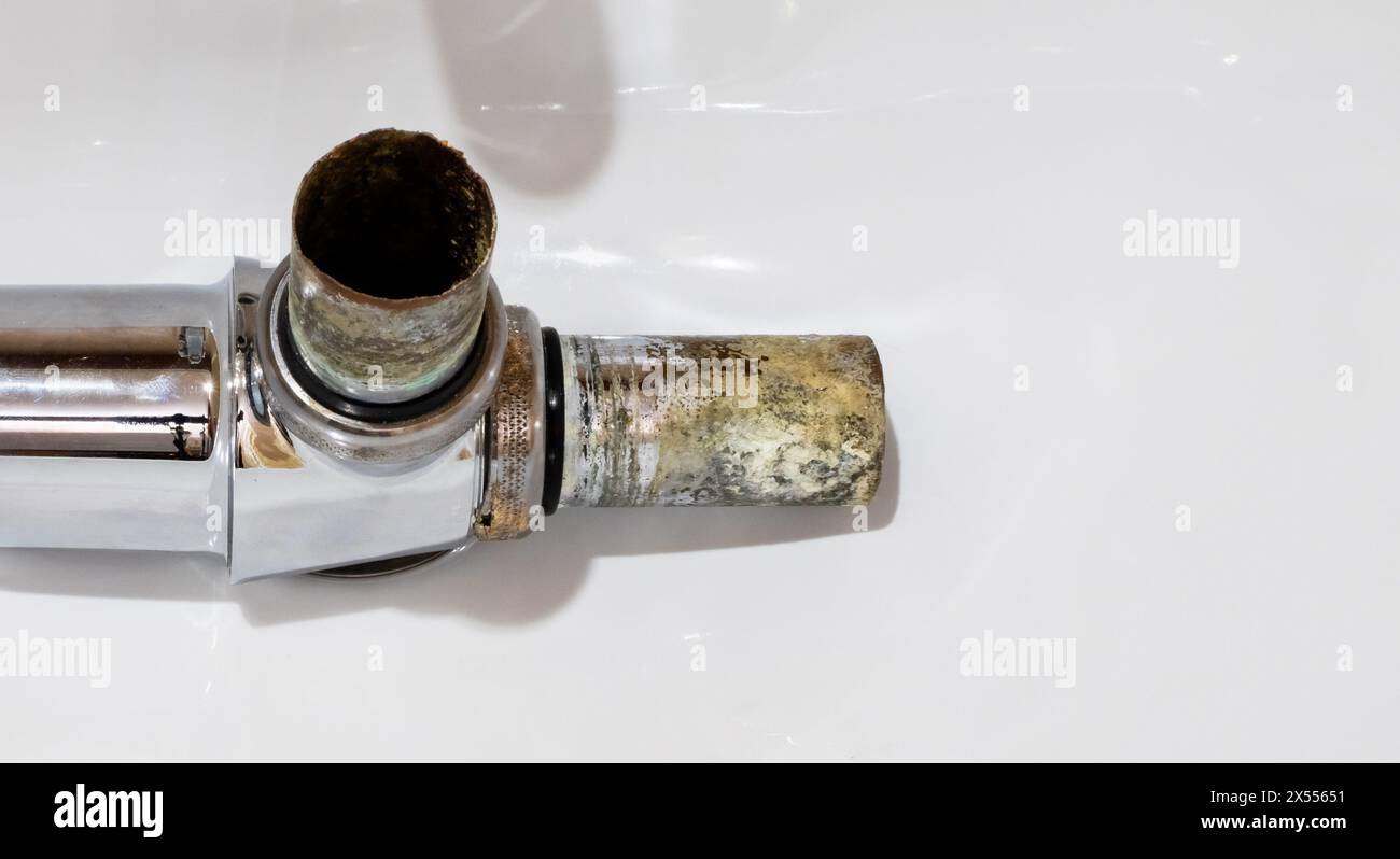 Metal drain siphon close-up with rusted pipes covered with corrosion on background of white ceramic sink Stock Photo