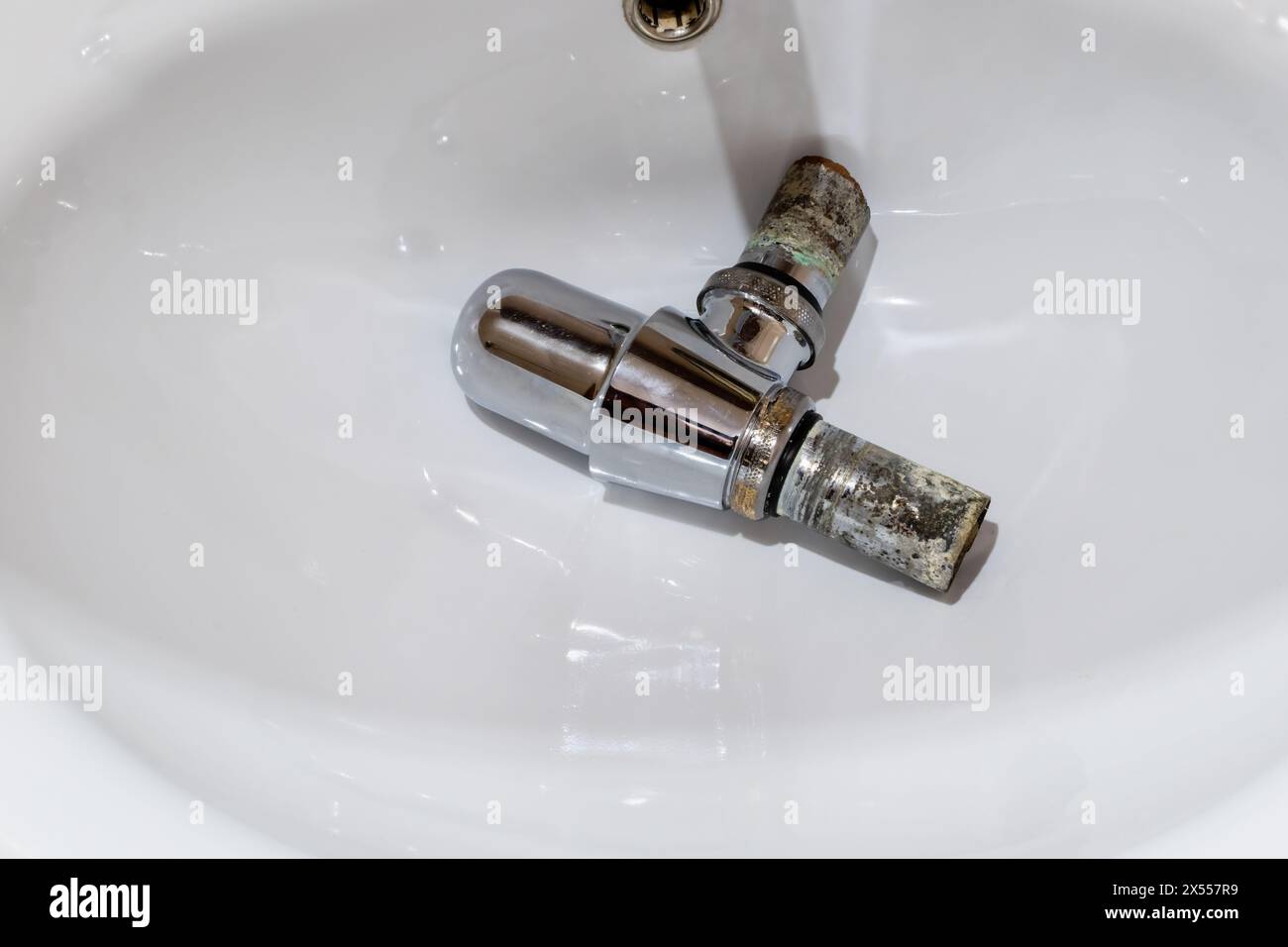 Metal drain siphon with rusted pipes covered with corrosion on background of white ceramic sink Stock Photo