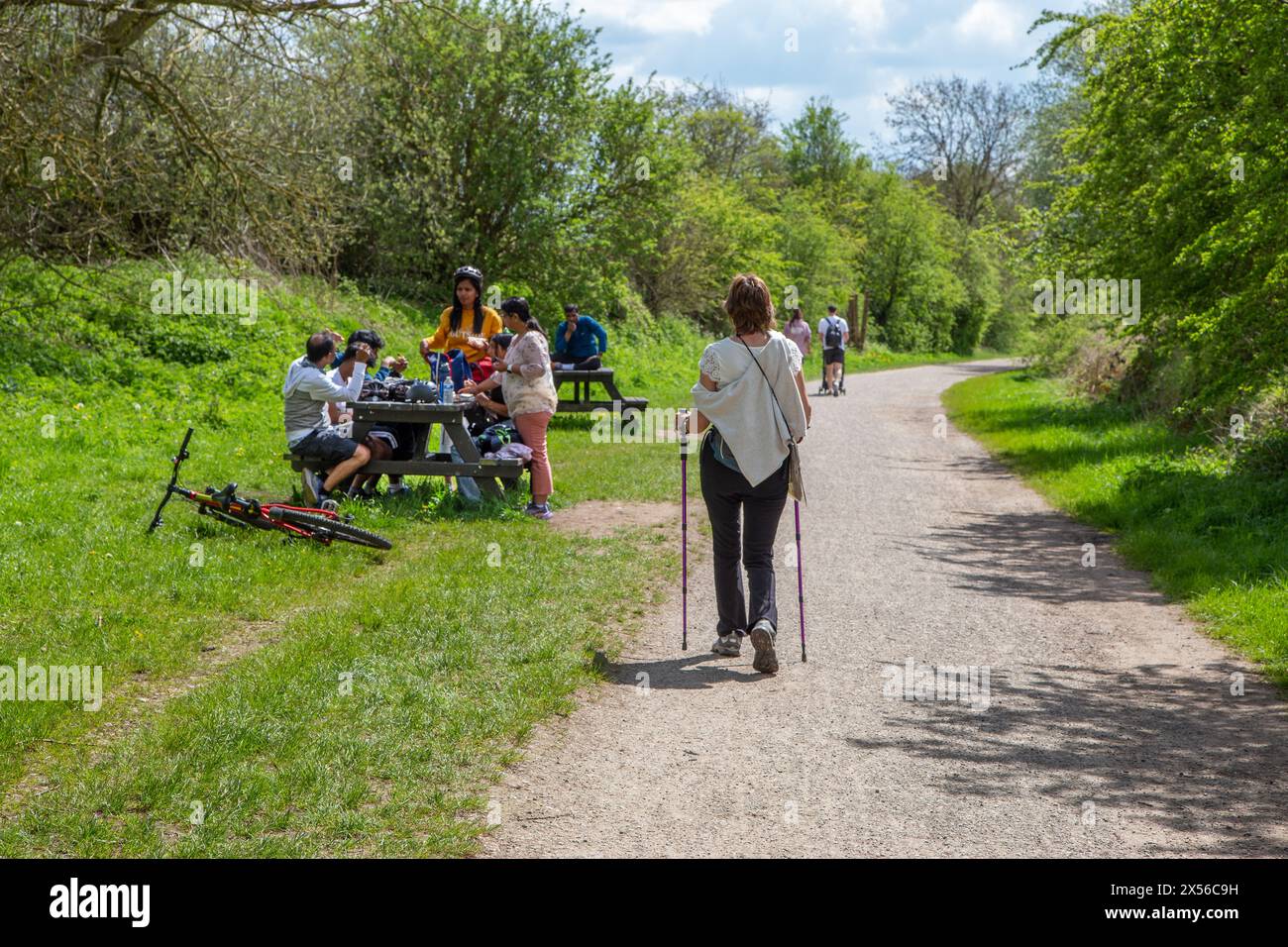 Woman walking rambling hiking past people picnicking while walking  on the Monsal trail footpath using the disused railway line in the Peak District Stock Photo