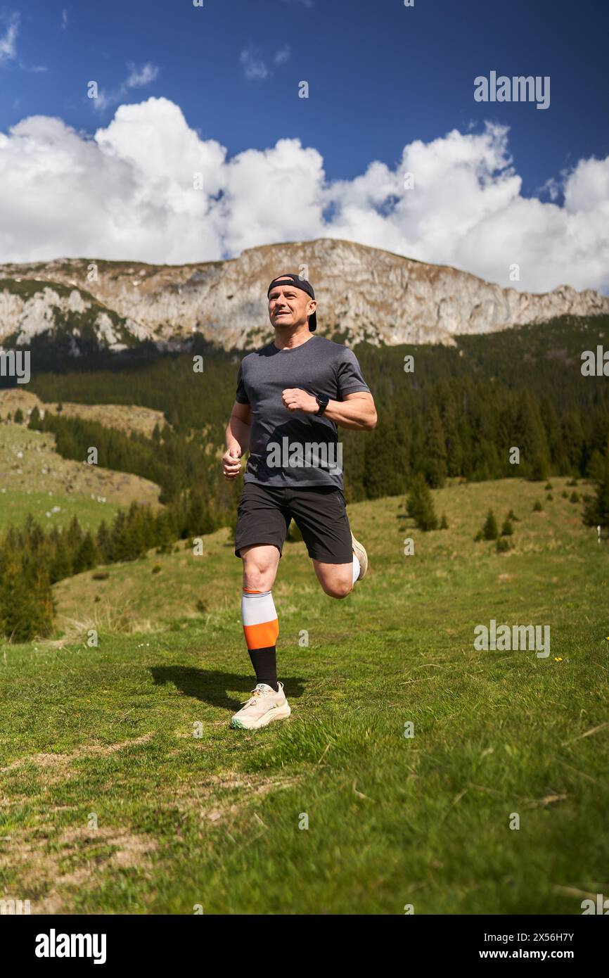 Trail runner in a race running with mountains behind on a meadow Stock Photo