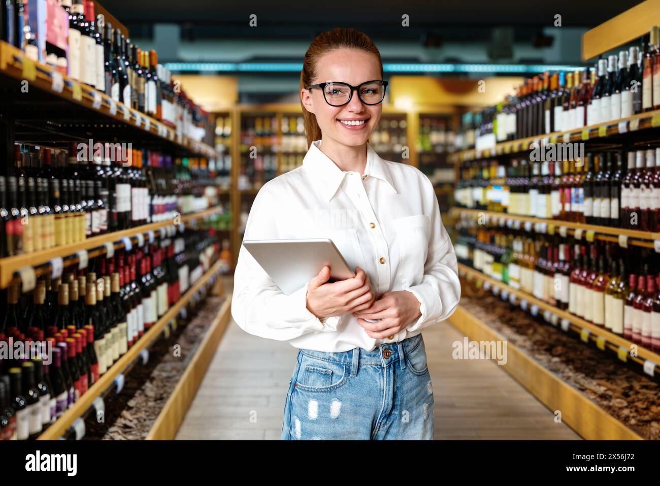 Woman retail manager with digital tablet in her hands stands in wine liquor store and smiling. Businesswoman works in retail. Stock Photo
