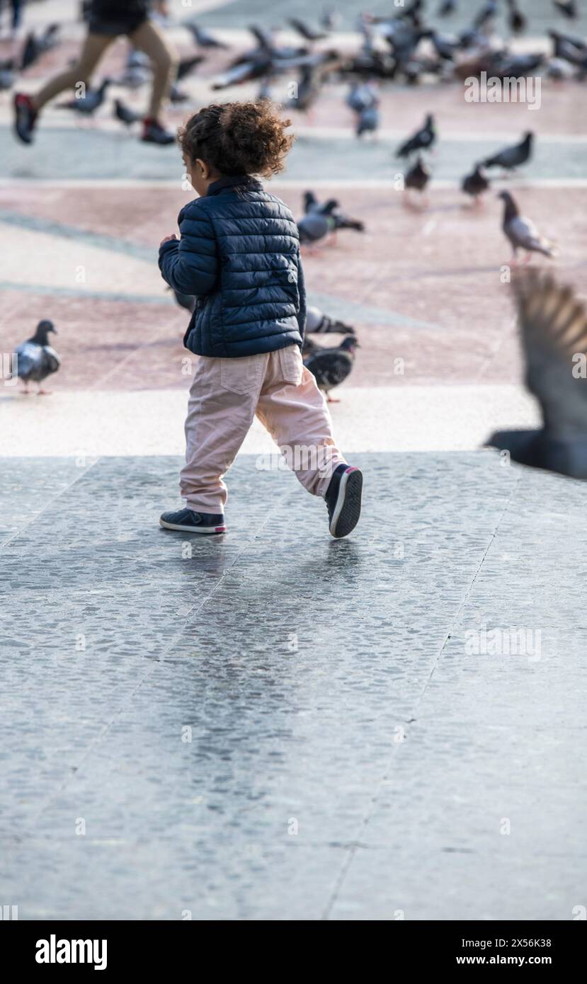 Young girl chasing pigeons in a public square Stock Photo