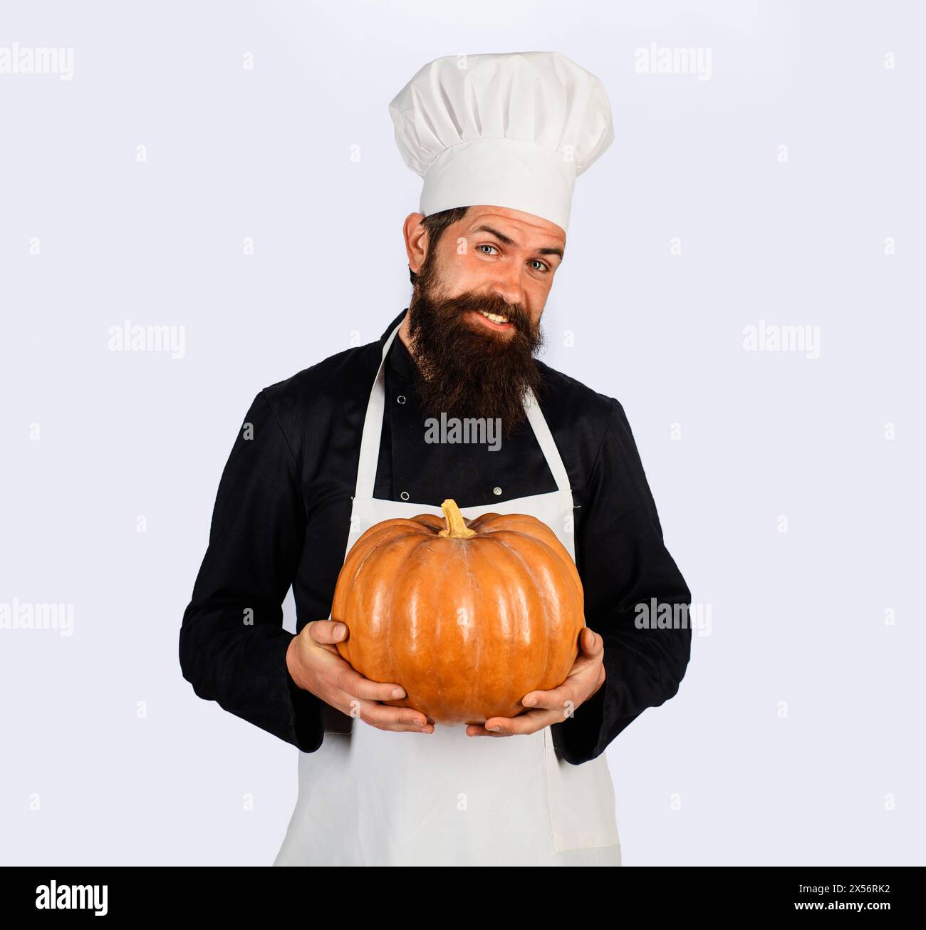 Smiling male chef in white apron with pumpkin. Organic food. Harvest festival. Bearded man in chef uniform with pumpkin. Thanksgiving day cooking Stock Photo