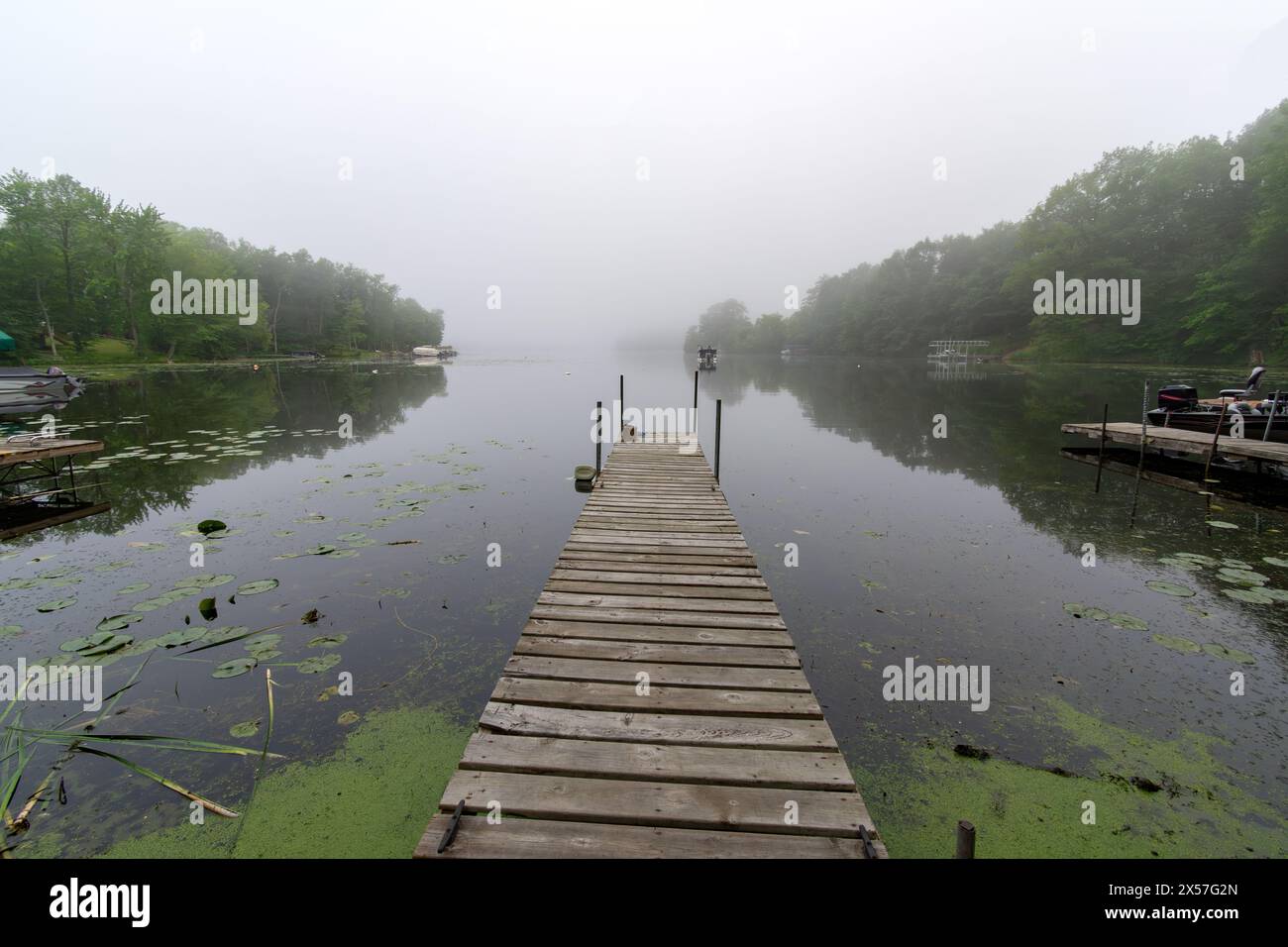 Looking down a pier on a calm Wisconsin lake on a foggy morning.  Fishing boat in distance. Stock Photo