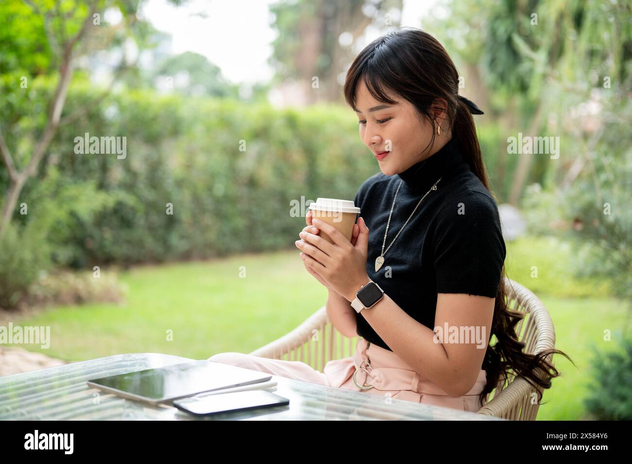 A beautiful, positive Asian woman sits at an outdoor table in a green ...