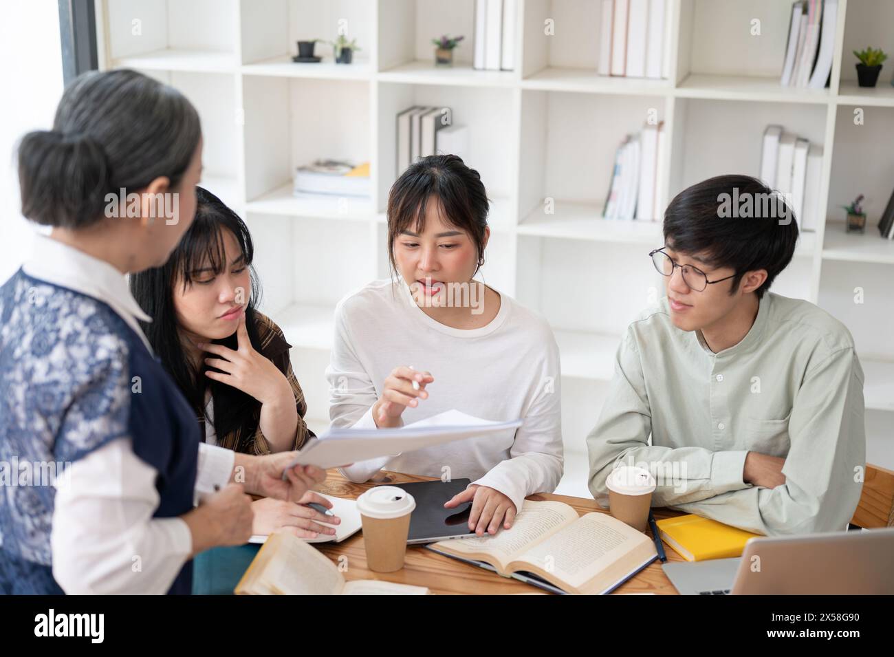 A group of young Asian university students is studying math with a senior professor in the classroom, listening to their professor explain the math pr Stock Photo