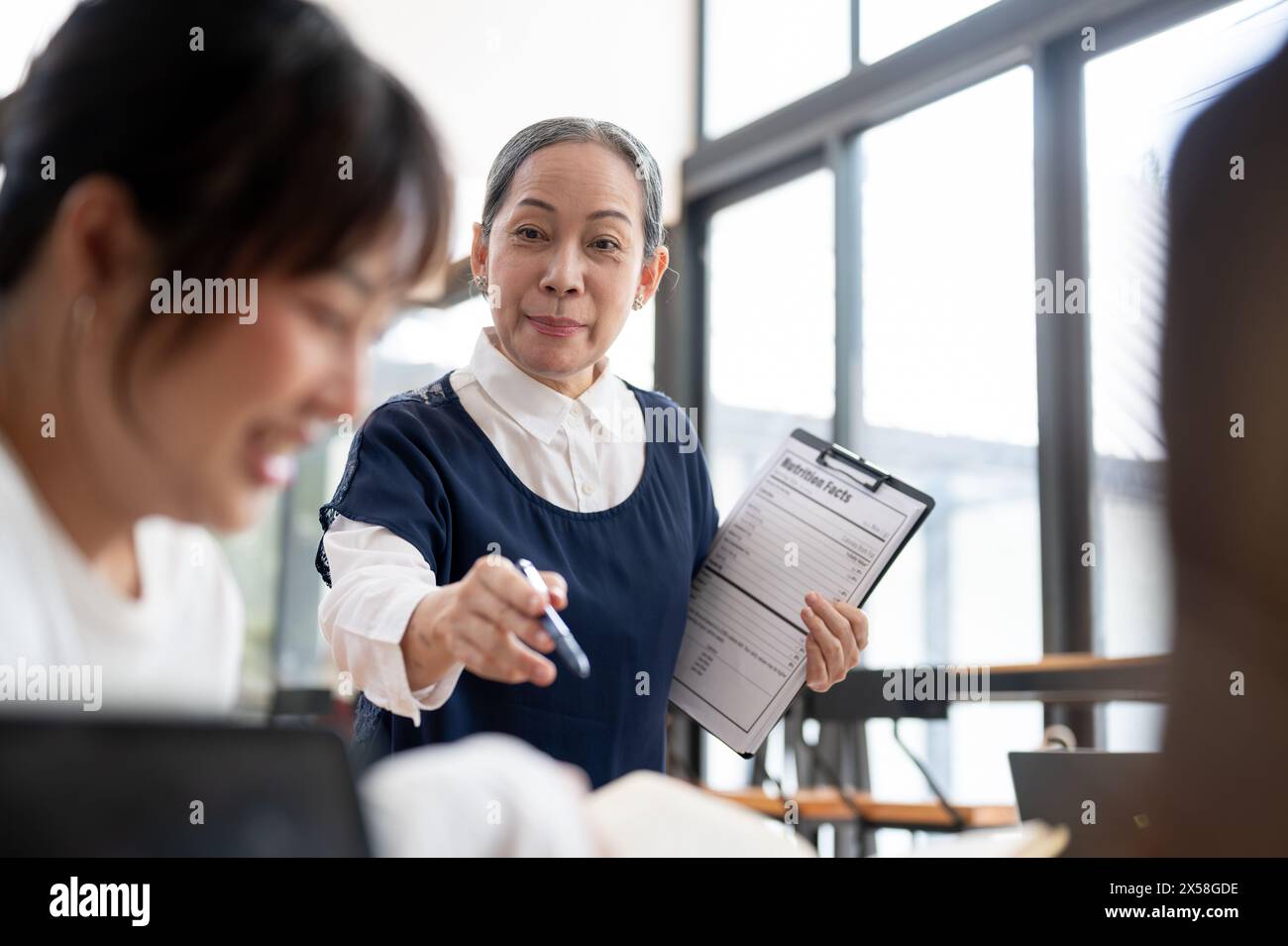 A mature Asian female teacher teaching students in the classroom, explaining a lesson to the students. Education concept Stock Photo