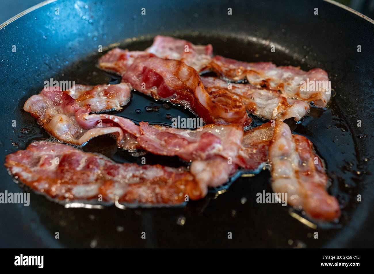 Frying bacon slices in frying pan on stove Stock Photo