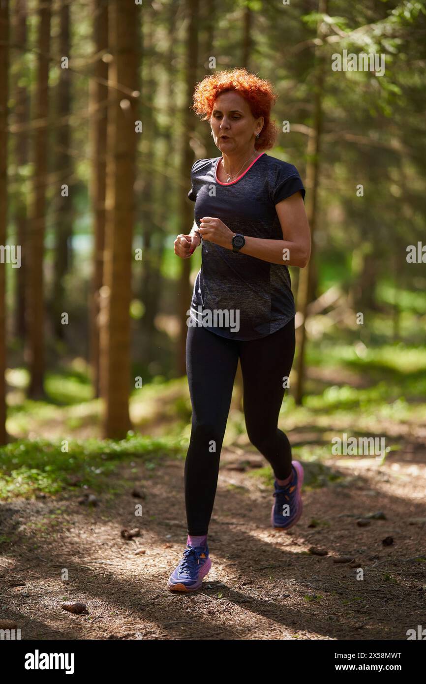 Redhead woman trail runner training in the forest running uphill Stock Photo
