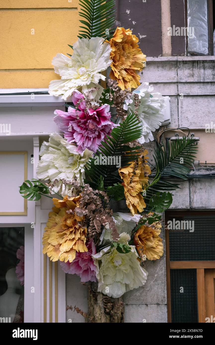 A cascade of handcrafted flowers adorns an urban facade, blending vibrant artistry with the architectural textures of city life. Stock Photo