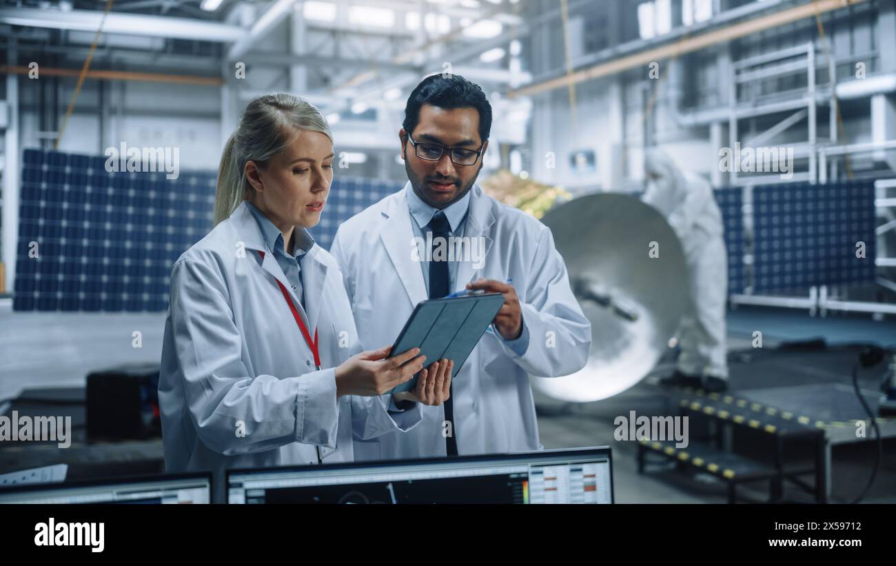 Two Engineers Talk, Use Tablet Computer while Working on Satellite ...