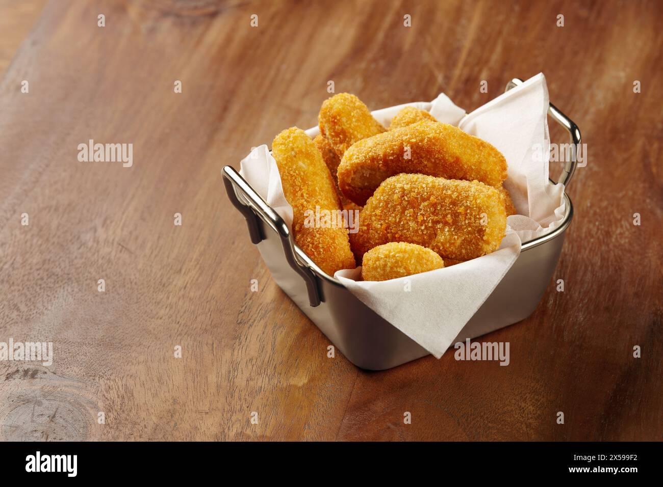 A portion of chicken nuggets served in a unique tin container with white napkin on a wooden table Stock Photo