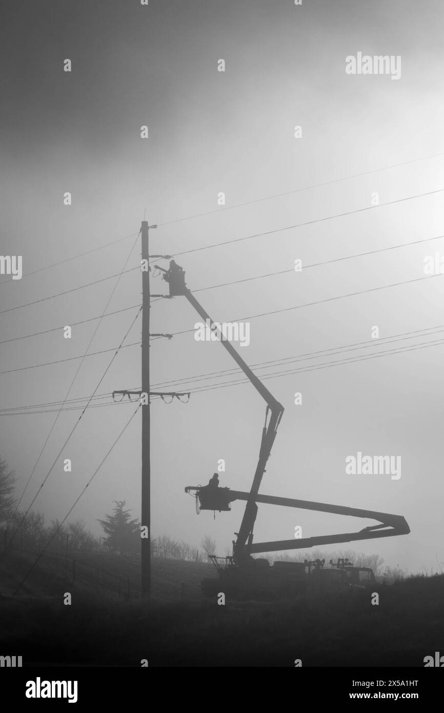 two utility workers working on a powerline in the fog Stock Photo