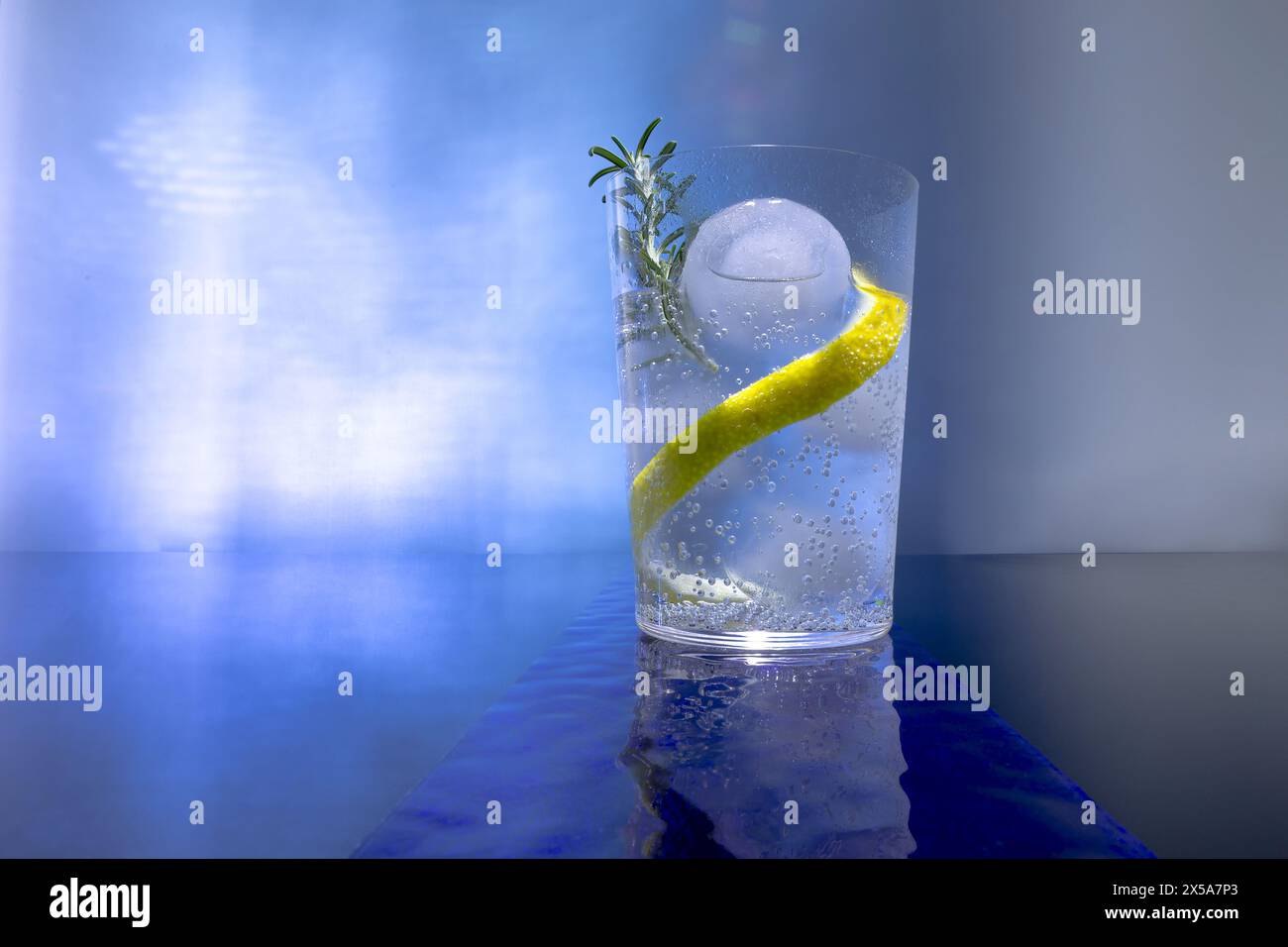 Refreshing gin tonic with ice sphere and lemon peel garnish on blue background Stock Photo