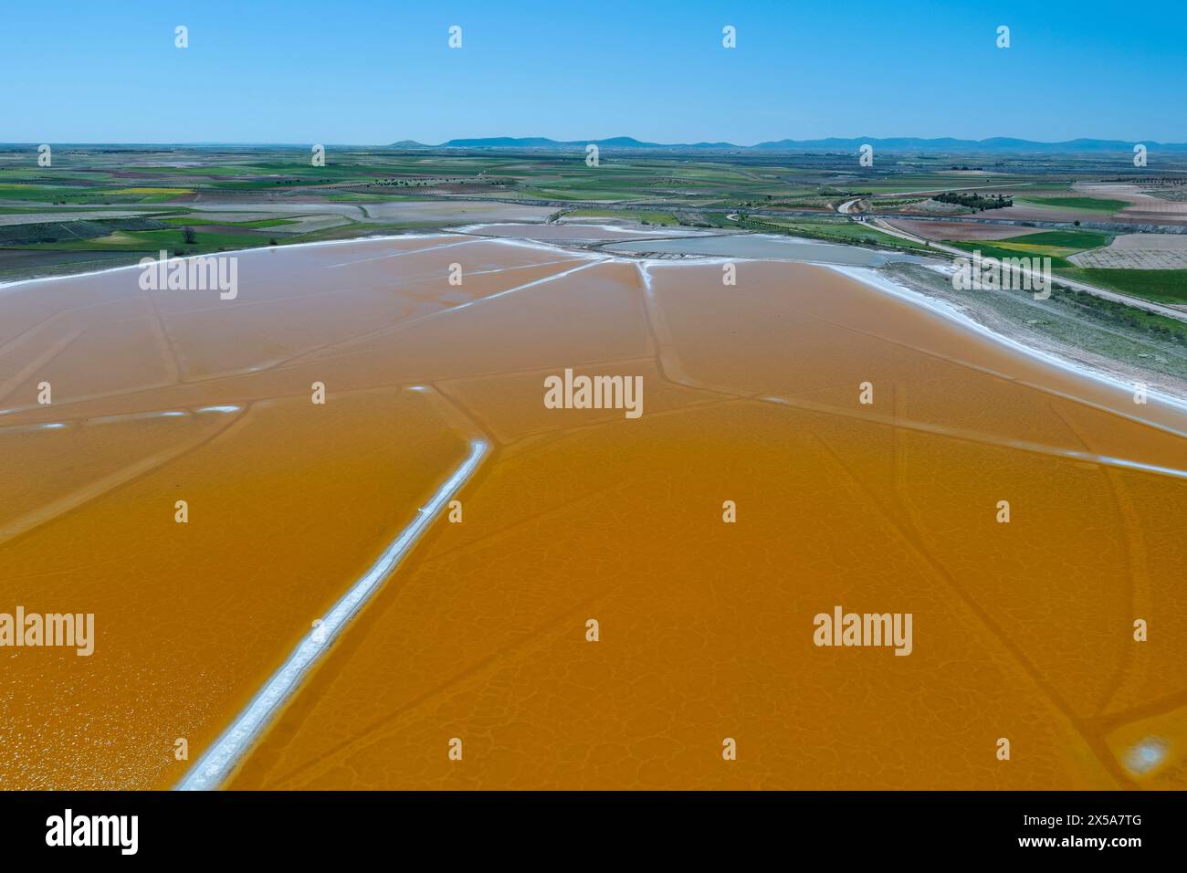 An aerial shot of serene salt lagoons with distinctive amber hues, set against the scenic backdrop of the Toledo countryside in Spain Stock Photo