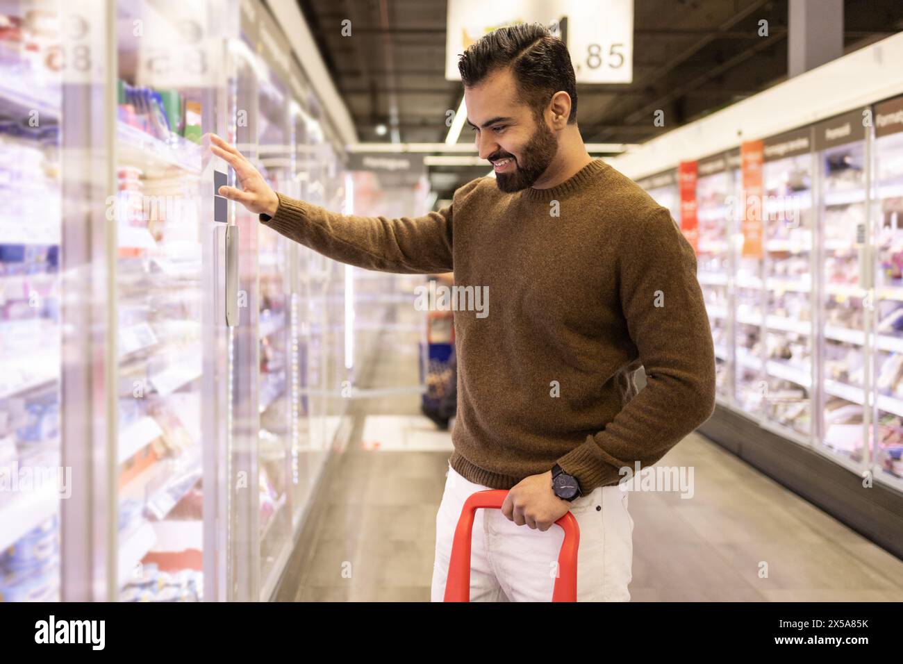 Smiling man selecting products in a supermarket freezer aisle Stock Photo