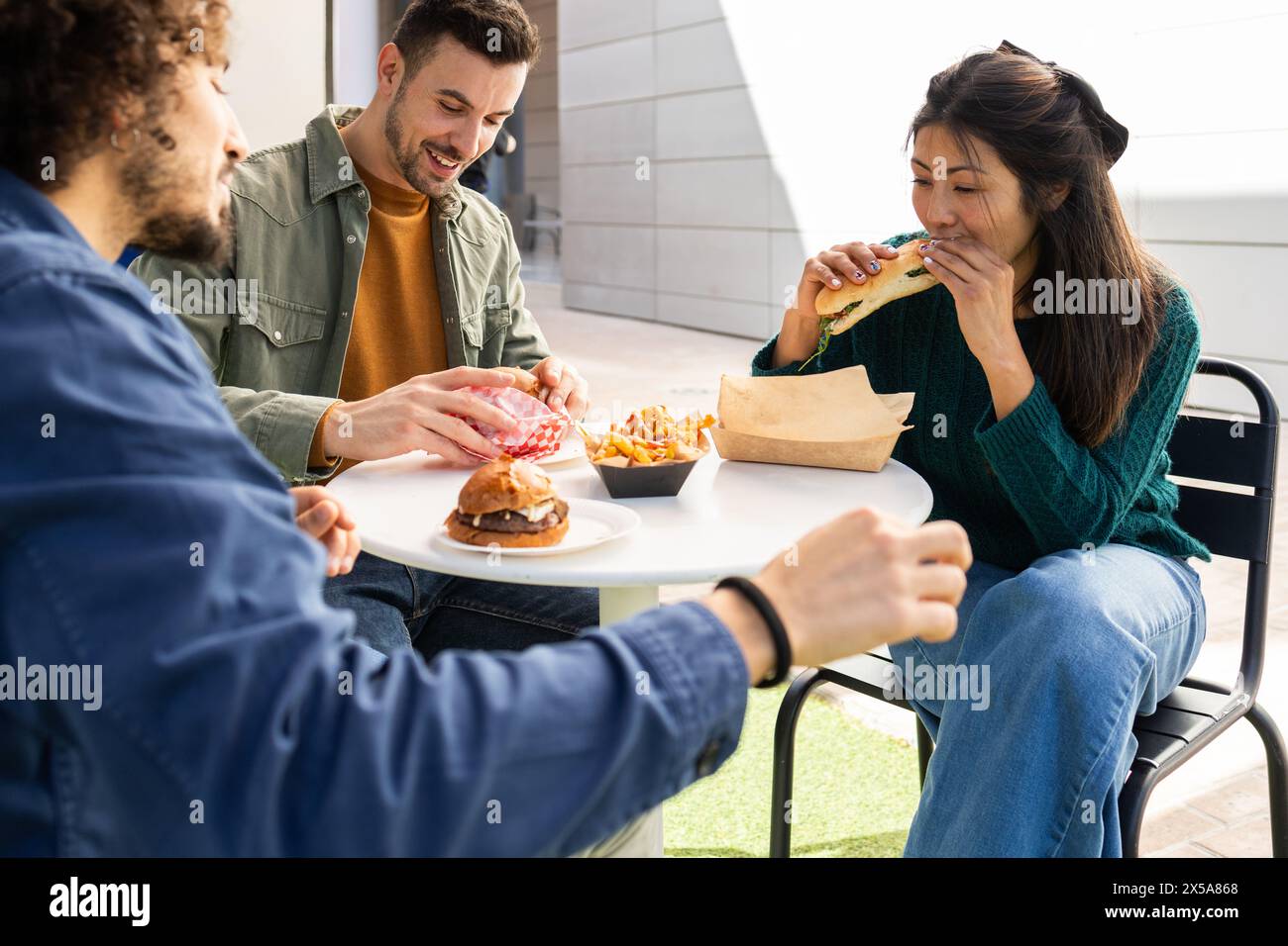 Group of friends enjoying fresh meals from a food truck at an outdoor seating area Stock Photo
